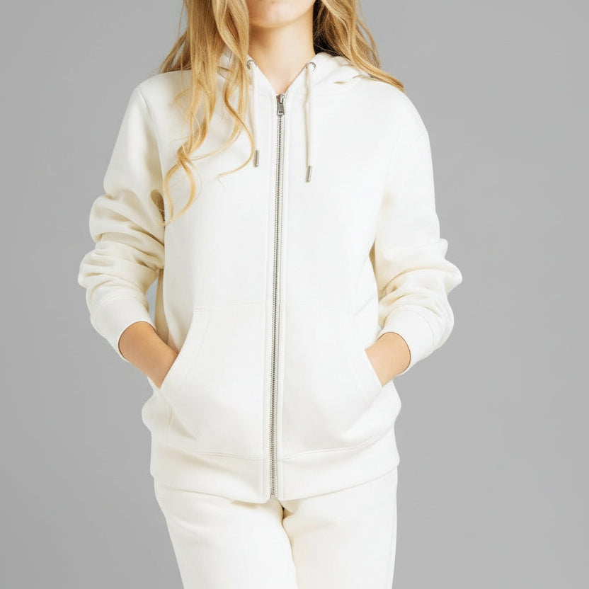 Blonde Caucasian female model standing next to a cactus wearing a cream colored pull over hoodie and a pair of matching sweatpants.