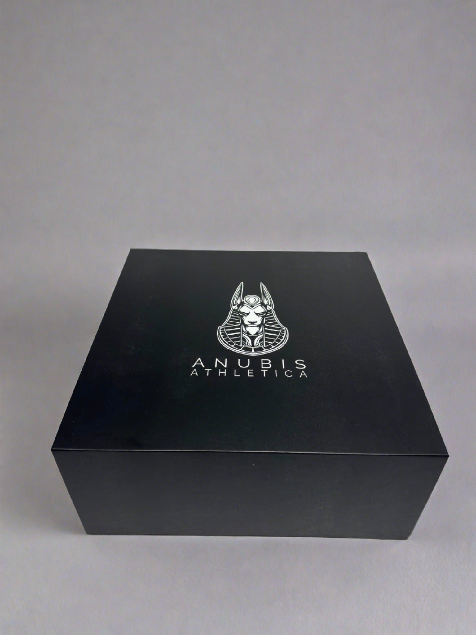 An example of the box the apparel is shipped in. The box is shiny black with a print of the Anubis Athletica logo printed in the center which includes the picture of Anubis and the name of the company below it.