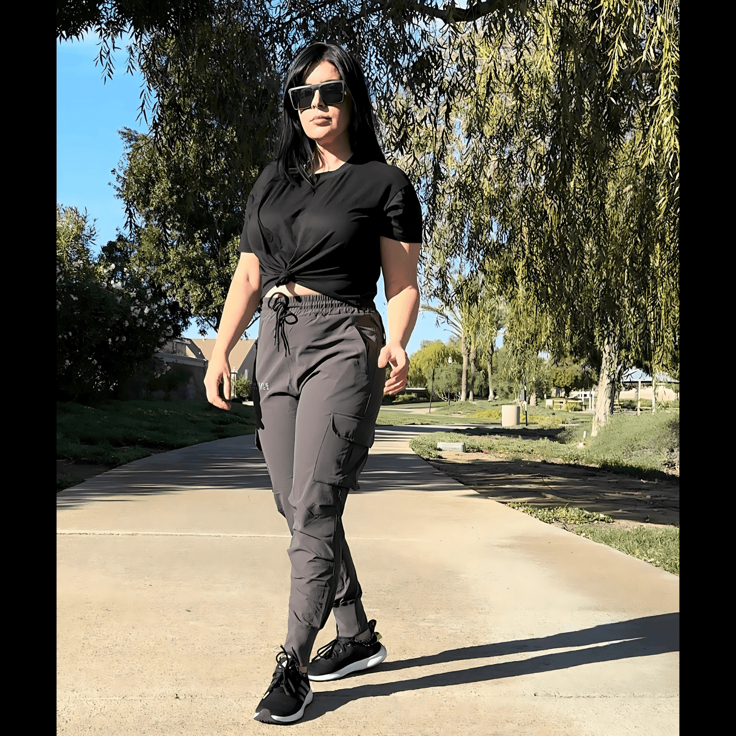 Woman in black top and gray pants walking on a path in a park.