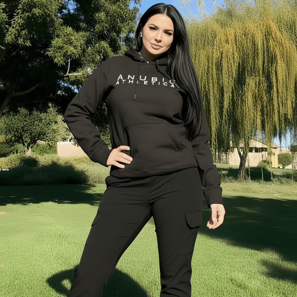 Woman wearing a black hoodie with 'ANUBIS ATHLETICAL' text in an outdoor setting.