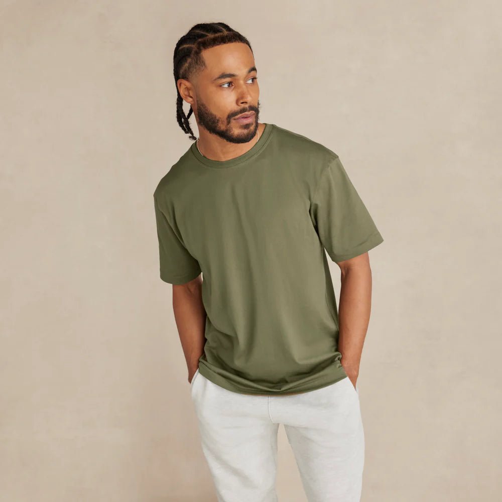 Man wearing an olive green t-shirt and white pants against a beige background