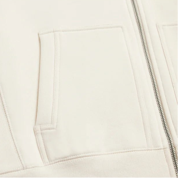 close up view of the pocket and zipper of a cream colored hoodie
