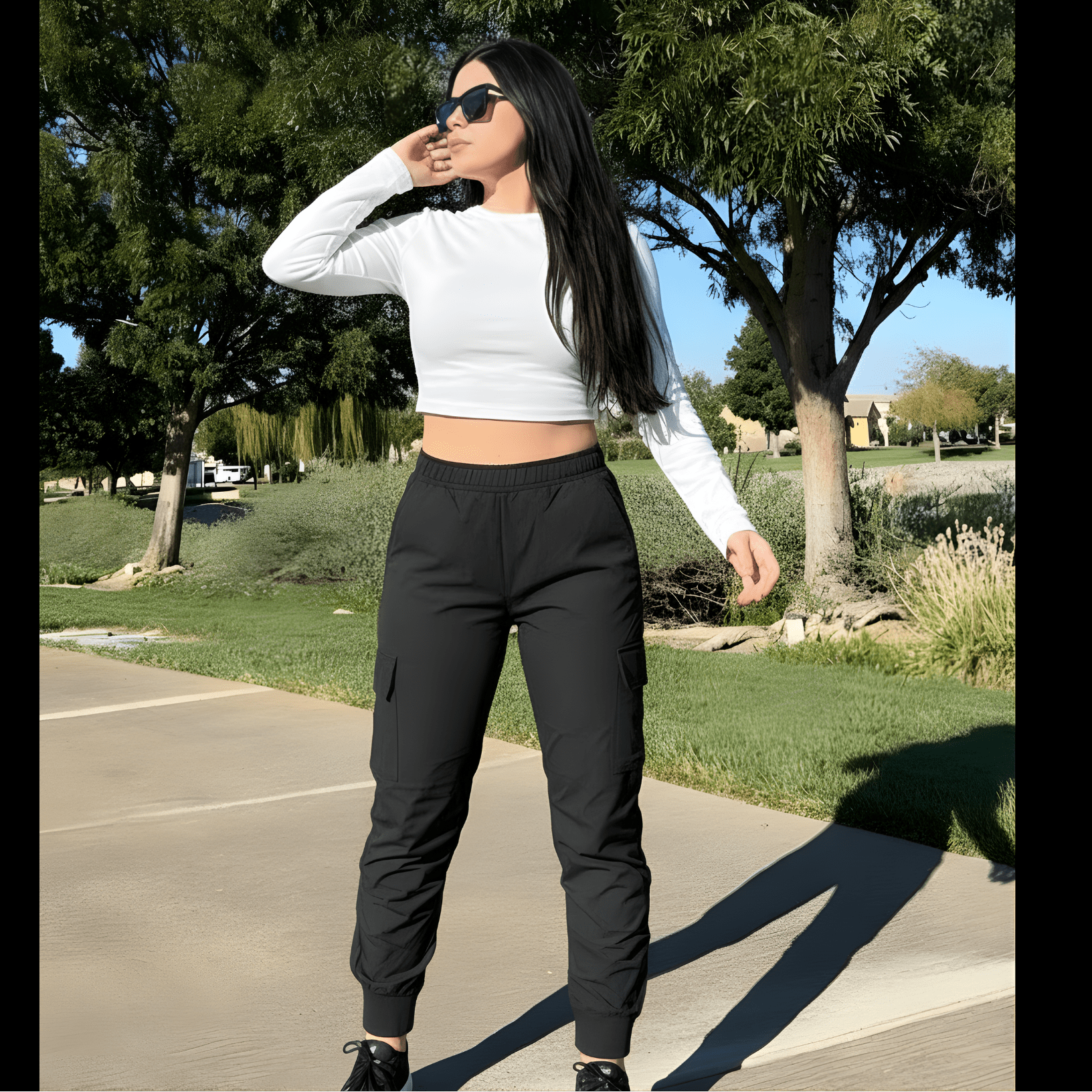Woman in a white crop top and black pants standing on a sidewalk with trees in the background