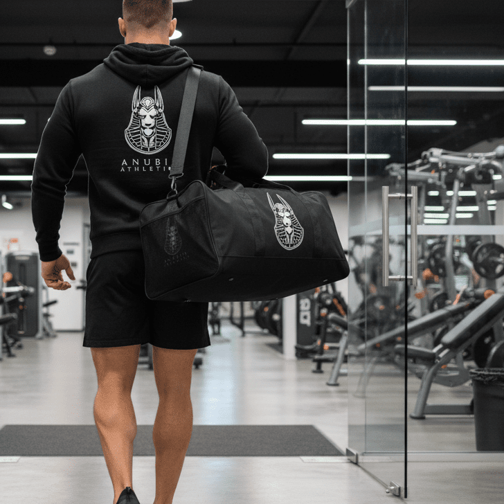 Man walking in a gym carrying a black duffel bag with branding.