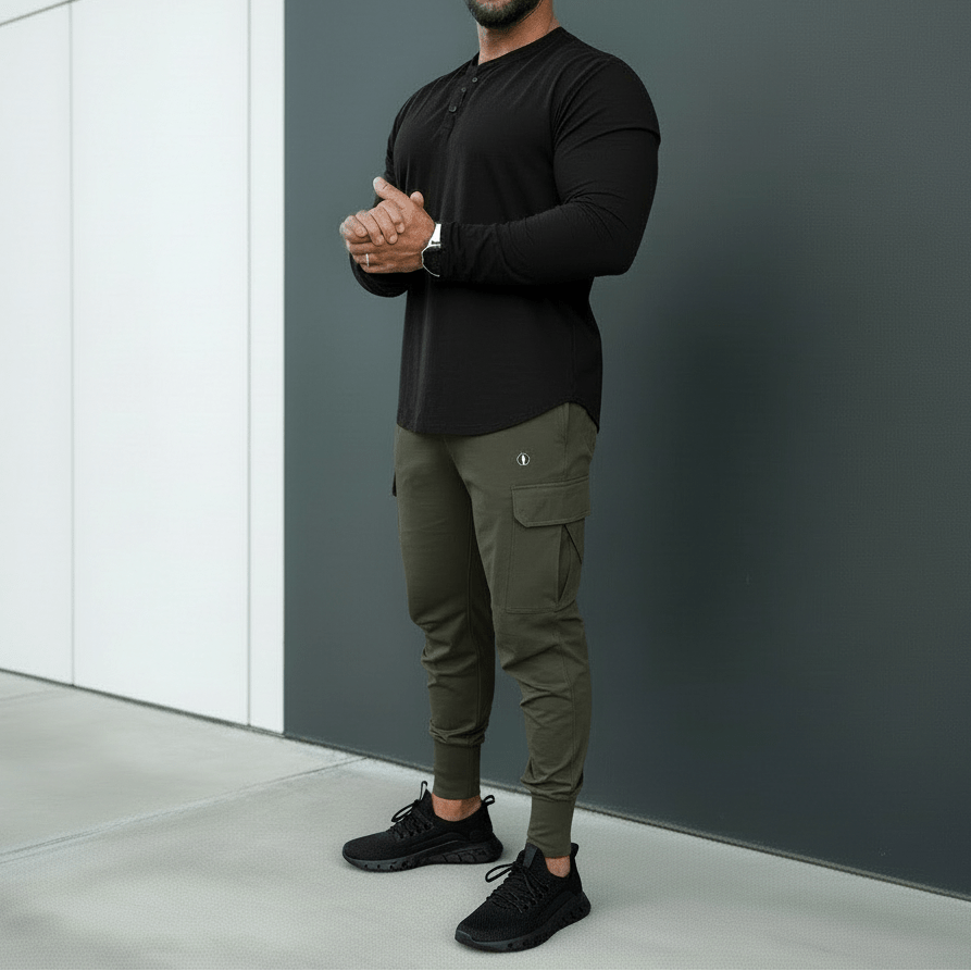 A man standing with arms crossed wearing black sunglasses, a black T-shirt, and black cargo joggers with multiple pockets.