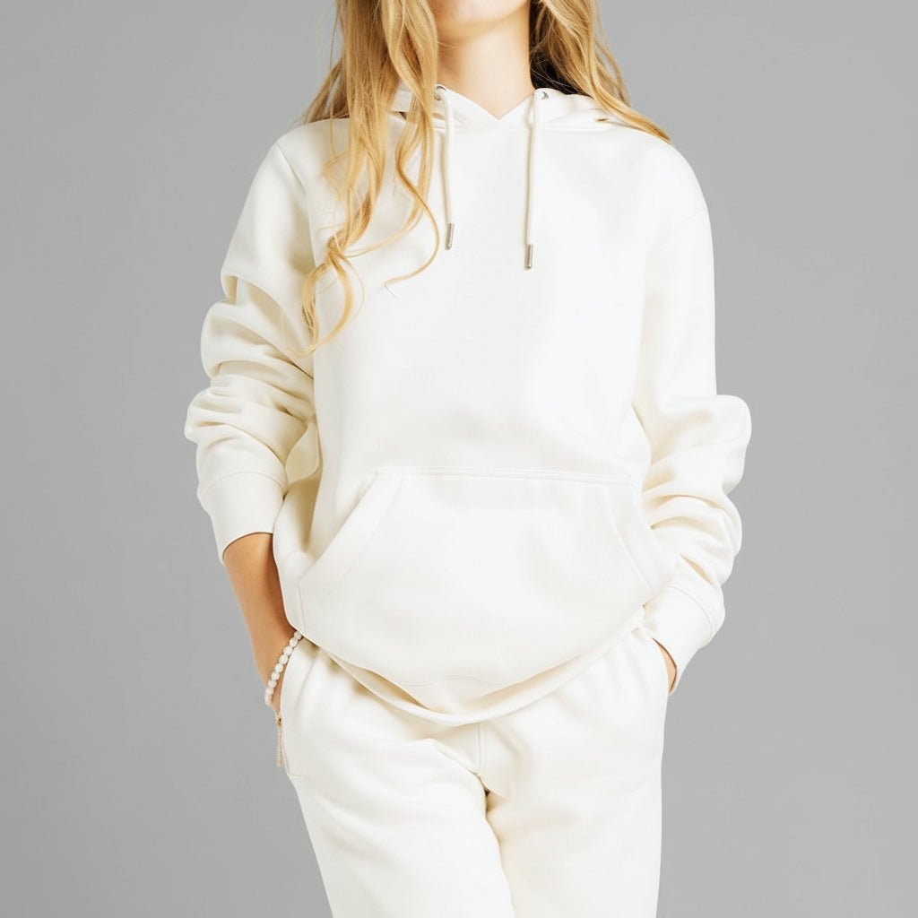 Blonde Caucasian female model standing next to a cactus wearing a cream colored pull over hoodie and a pair of matching sweatpants.