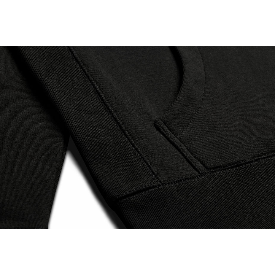 Close up view of the pocket on a black pull over hoodie.