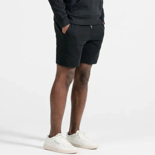 a black male model wearing a black pull over hoodie and matching sweat shorts from an angled view