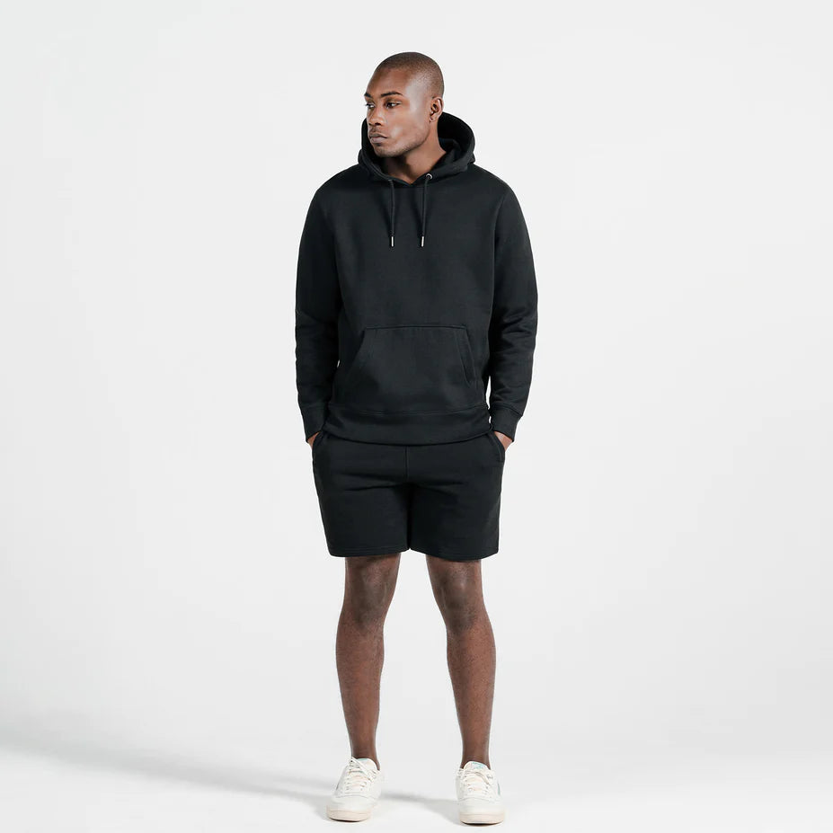 a black male model wearing a black pull over hoodie and matching sweat shorts