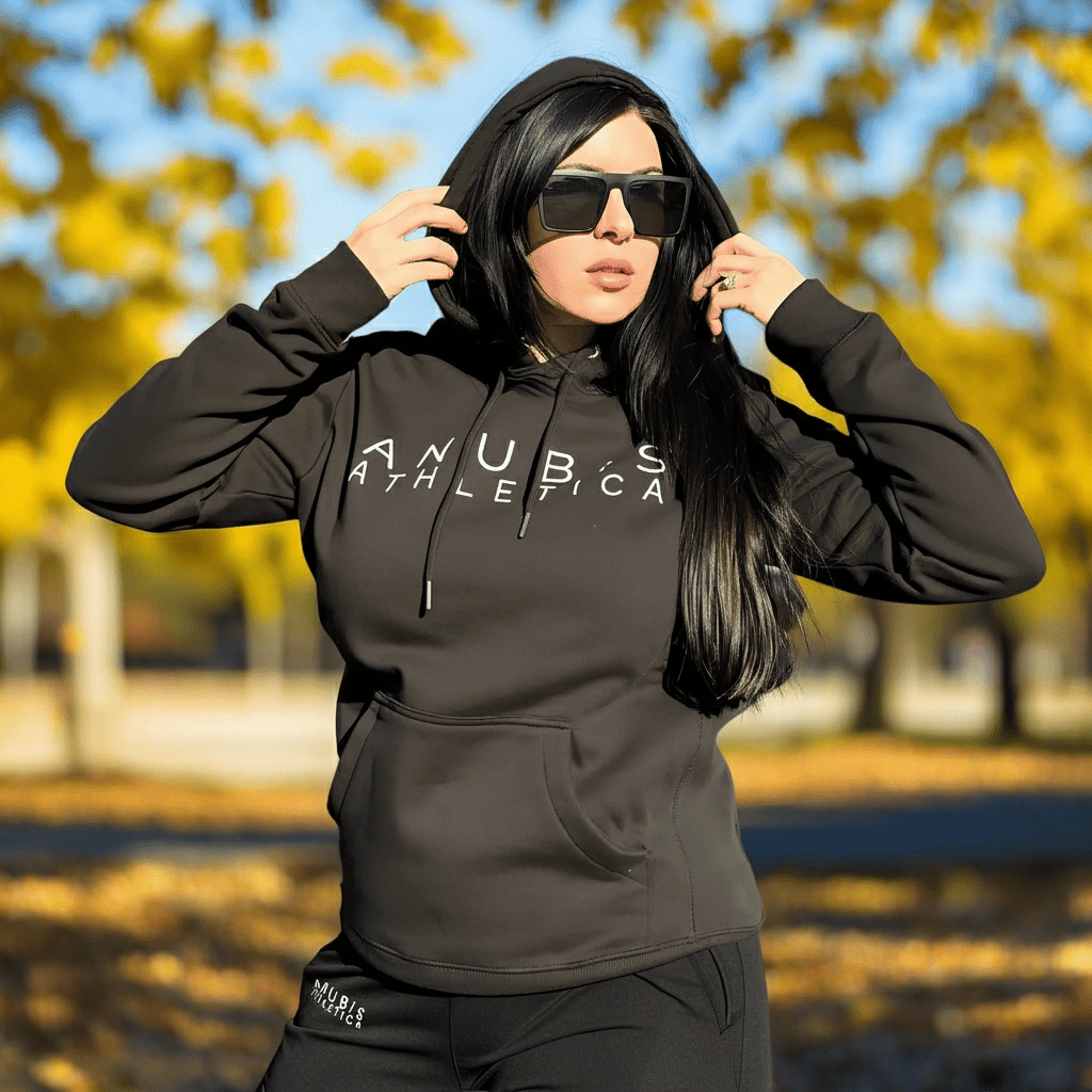 Person wearing a black hoodie with 'ANUBIS ATHLETICA' text, outdoors with blurred trees and sky.