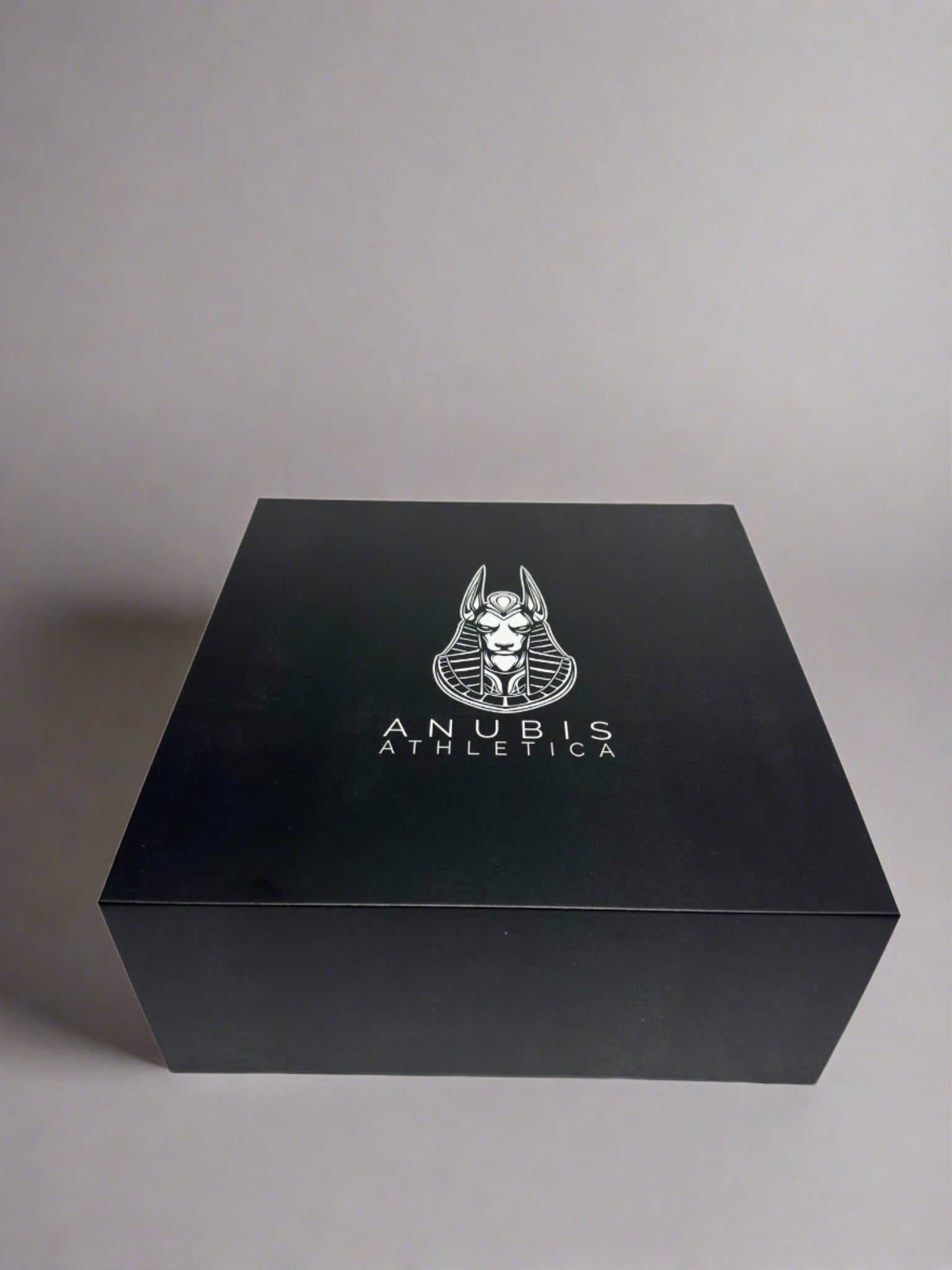 An example of the box the apparel is shipped in. The box is shiny black with a print of the Anubis Athletica logo printed in the center which includes the picture of Anubis and the name of the company below it.