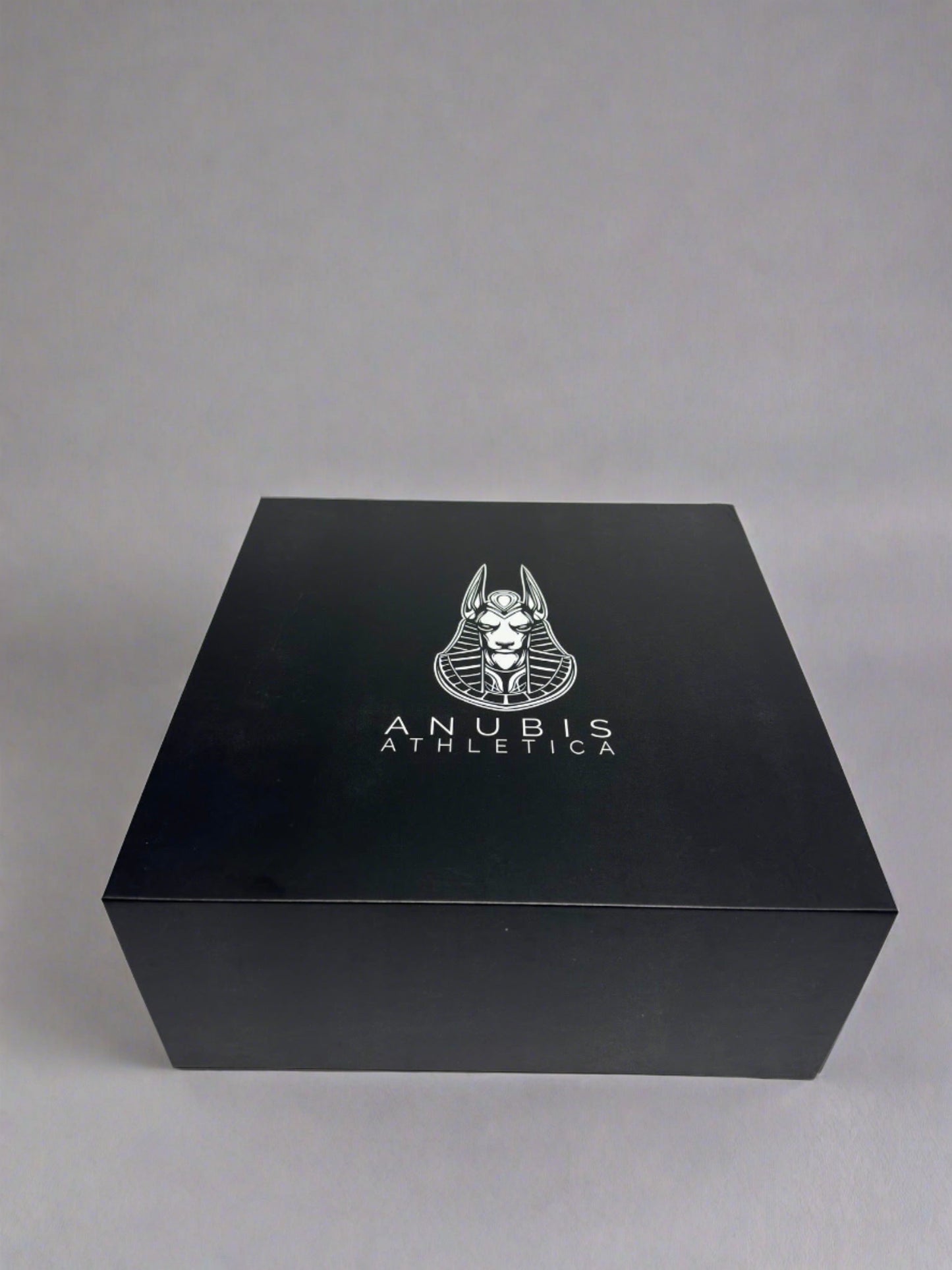 An example of the box the apparel is shipped in. The box is shiny black with a print of the Anubis Athletica logo printed in the center which includes the picture of Anubis and the name of the company below it. 