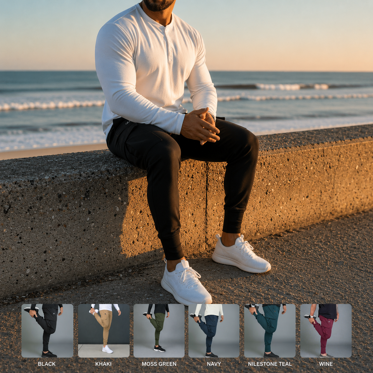 A man sits on a concrete ledge by the ocean wearing a white long-sleeve quarter-zip henley shirt and black jogger pants. The photo is taken in warm golden hour light, with ocean waves and sky in the background.