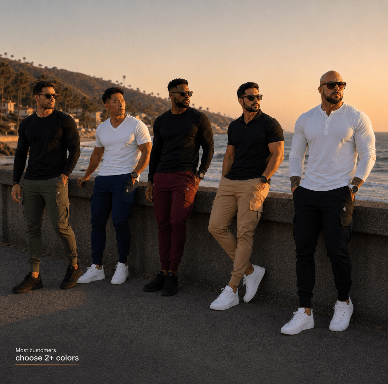 Five men wearing different casual shirts and pants stand together on a seaside walkway at sunset. The shirts shown are black, white, and dark blue, paired with olive green, navy, burgundy, tan, and black pants.