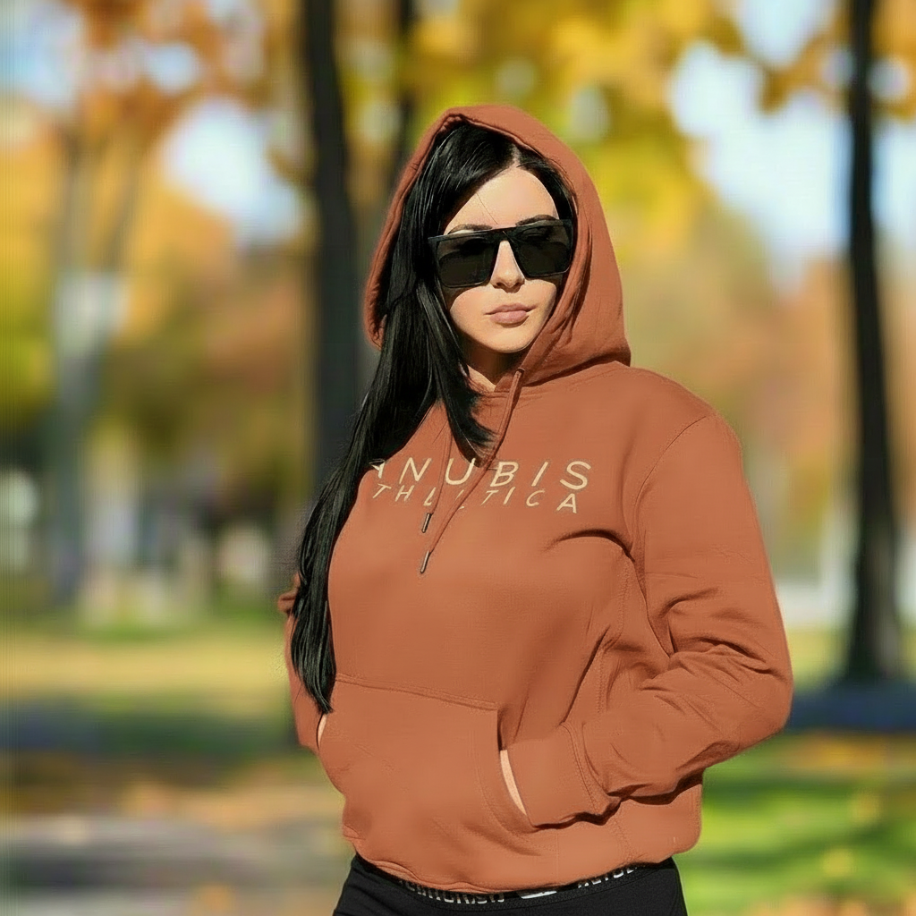 Person wearing a brown hoodie with 'ANUBIS ATHLETICA' text in an outdoor setting with trees and grass.
