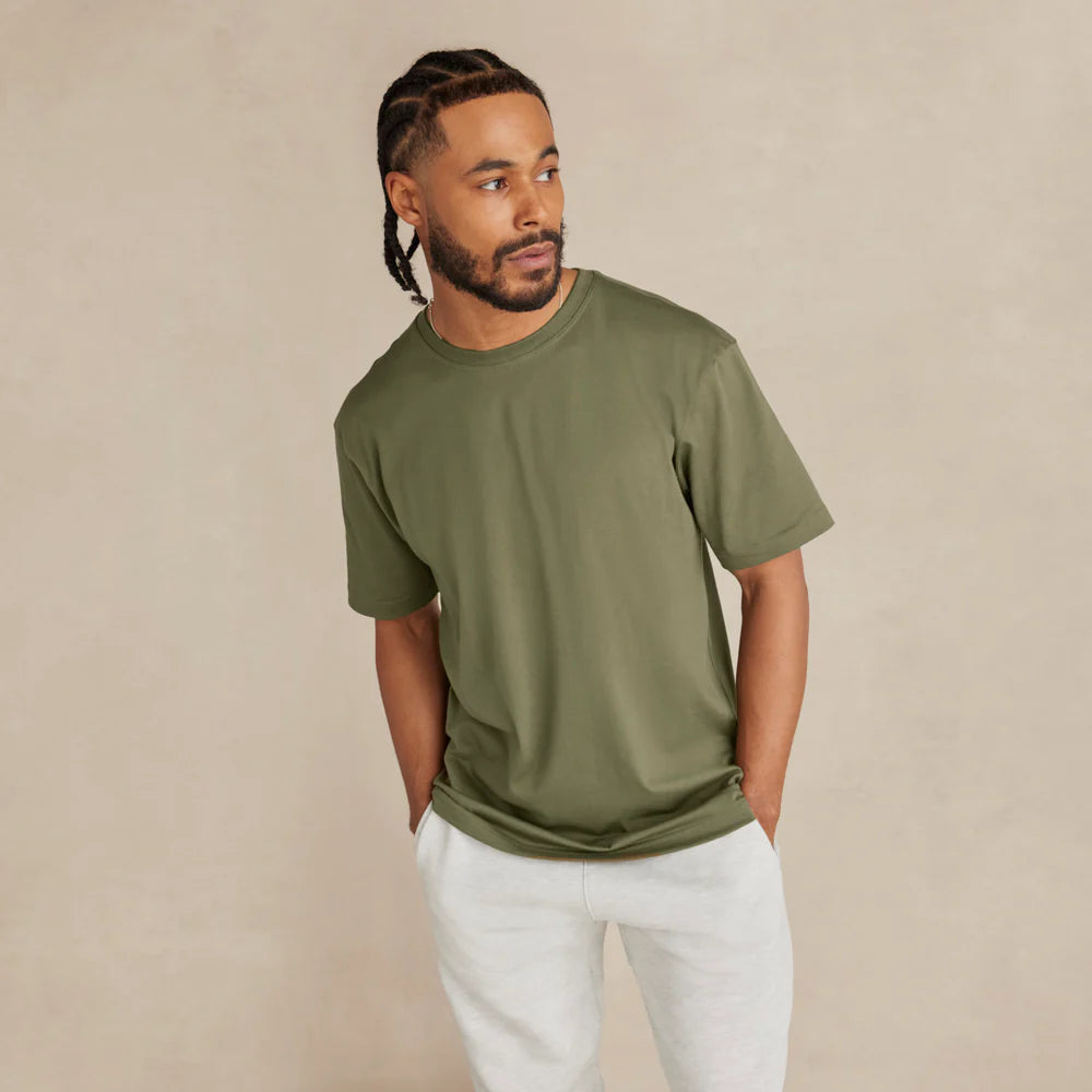 Man wearing an olive green t-shirt and white pants against a beige background