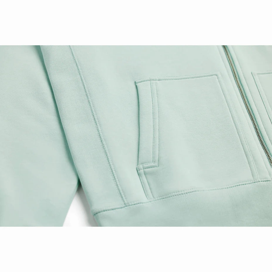 a close up view of a seafoam colored zip up hoodie showing the pocket and bottom of the zipper