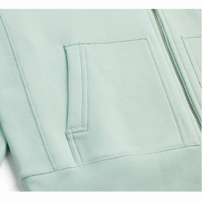 a close up view of a seafoam colored zip up hoodie showing the pocket and bottom of the zipper