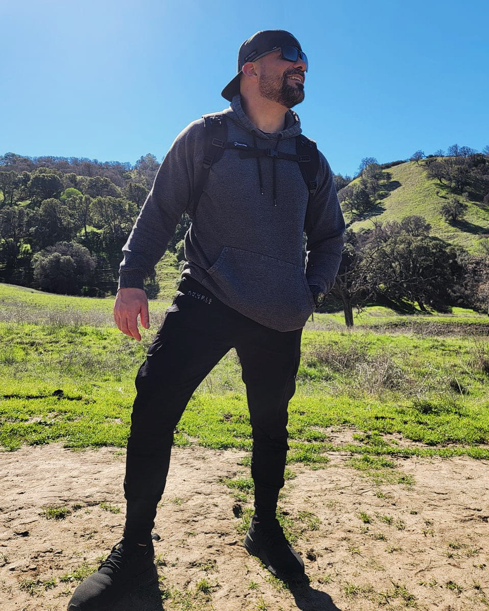 Male in the outdoors wearing a gray hoodie, black hat, and black cargo joggers