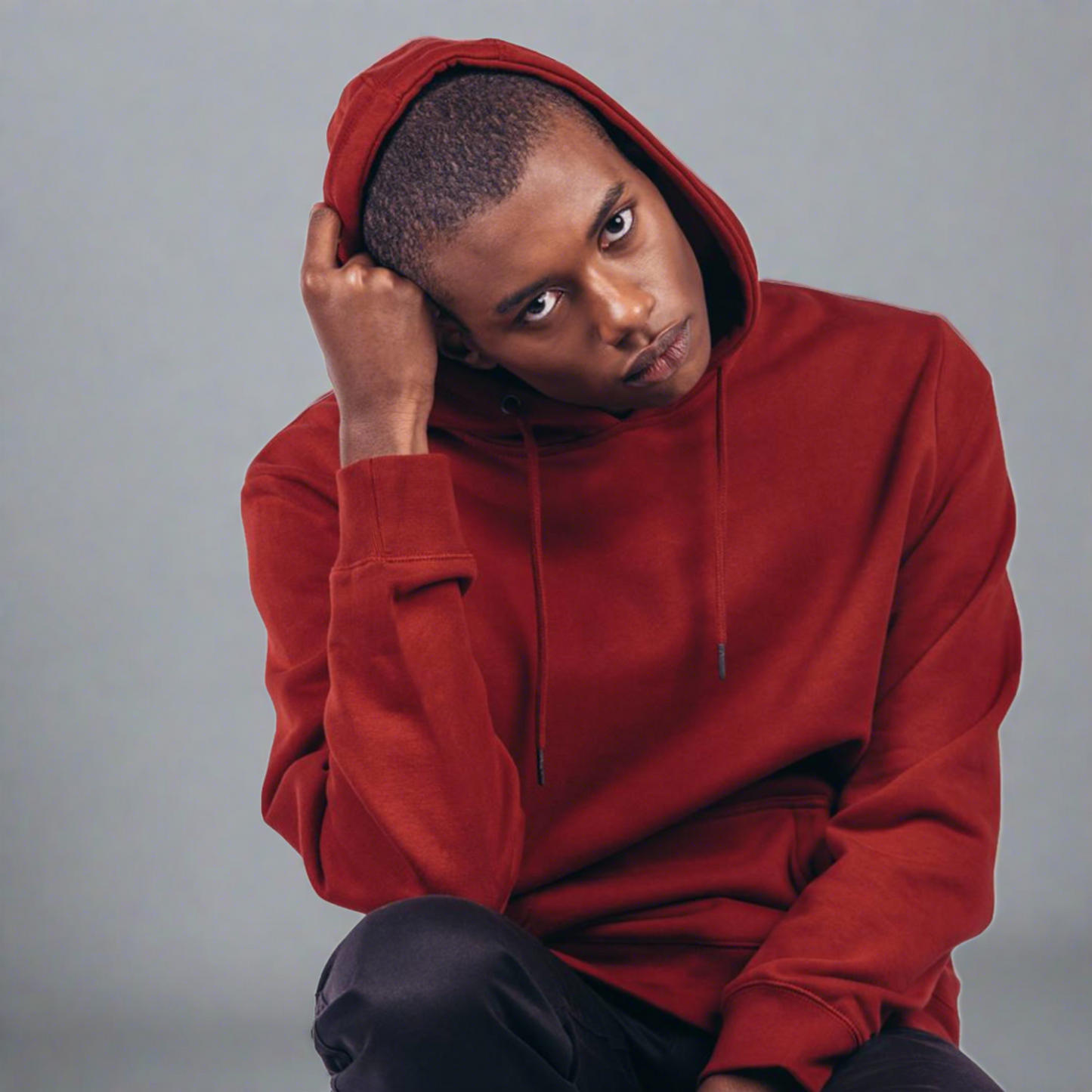 a black male model wearing an oxblood red pull over hoodie and black pants