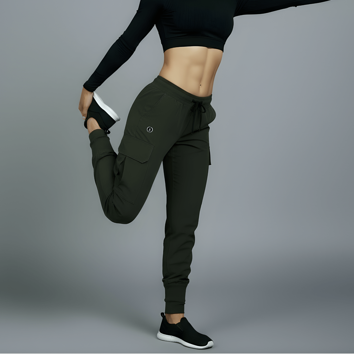 Woman in black athletic top and green leggings posing against a gray background